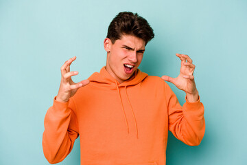 Young caucasian man isolated on blue background screaming with rage.
