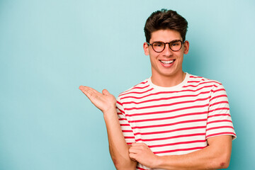 Young caucasian man isolated on blue background showing a copy space on a palm and holding another...