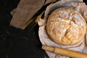 Fresh homemade crisp bread on Kraft paper with rye sticks and flour and over black table. Healthy baked bread on black wooden background.