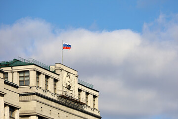 Russian flag on the parliament building in Moscow on background of blue sky and white clouds....