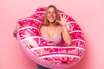 Young caucasian woman holding an air mattress isolated on pink background smiling cheerful showing...