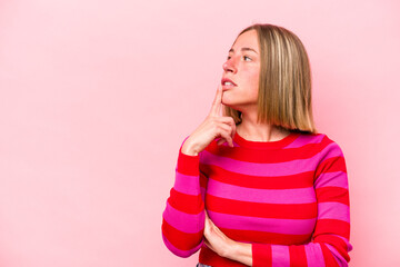 Young caucasian woman isolated on pink background looking sideways with doubtful and skeptical expression.