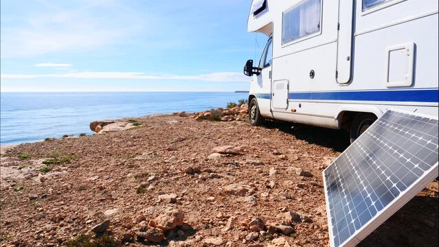 Time lapse of clouds moving across sky over portable solar panel at camper vehicle on sea coast. Renewable free energy on caravan vacation.