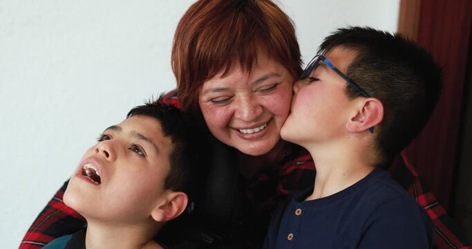 Happy mother having tender moment with her two sons at home - Child care with disability concept