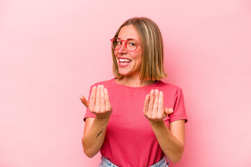Young caucasian woman isolated on pink background pointing with finger at you as if inviting come closer.