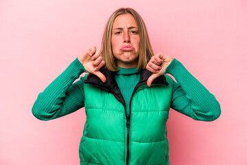 Young caucasian woman isolated on pink background showing a dislike gesture, thumbs down....