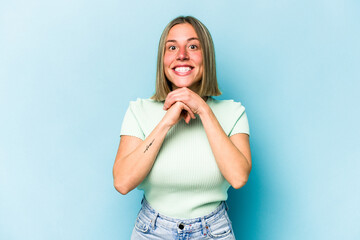 Young caucasian woman isolated on blue background praying for luck, amazed and opening mouth looking to front.