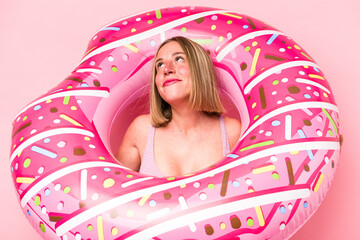 Young caucasian woman holding air mattress isolated on pink background
