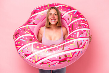 Young caucasian woman holding air mattress isolated on pink background