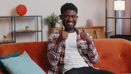 African american man looking at camera with toothy smile, raises thumbs up agrees with something or...
