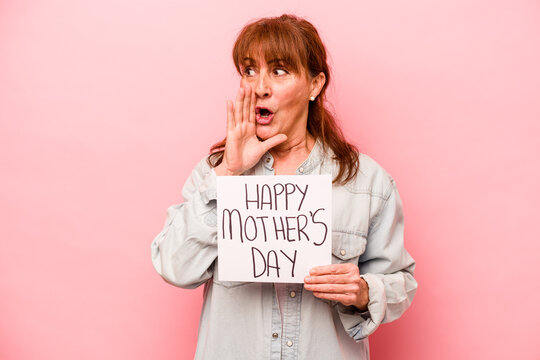 Middle age caucasian woman holding Happy mother’s day placard isolated on pink background is saying a secret hot braking news and looking aside