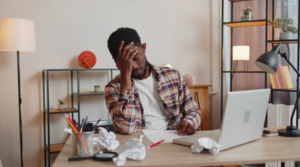 Tired African American man freelancer teacher use laptop computer, suffering from tension migaine headache after e-learning remote working job with pupils sitting at home office table. Guy businessman