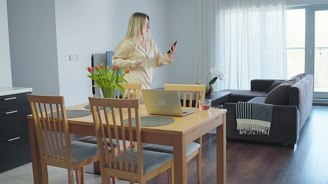 Young woman using smartphone dancing and listening to music. Social distancing, internet, chatting concept. WFH reality. Stay at home. Weekend, Holidays time