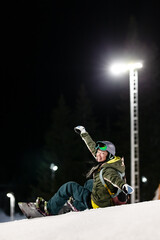 Snowboarder girl posing on slopes. Night skiing in winter resort..