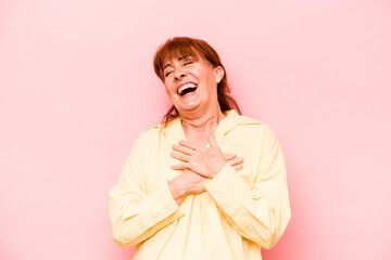 Middle age caucasian woman isolated on pink background laughing keeping hands on heart, concept of...