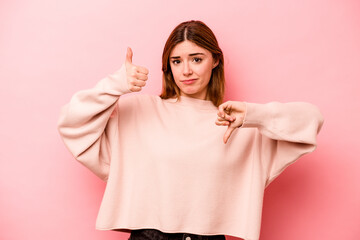 Young caucasian woman isolated on pink background showing thumbs up and thumbs down, difficult...