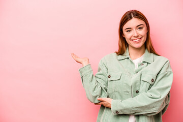 Young caucasian woman isolated on pink background showing a copy space on a palm and holding another hand on waist.