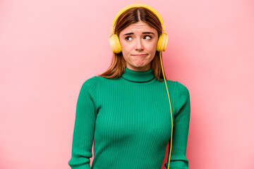 Young caucasian woman listening to music isolated on pink background confused, feels doubtful and unsure.