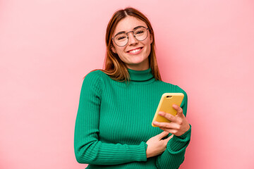 Young caucasian woman holding mobile phone isolated on pink background laughing and having fun.