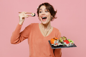 Young happy excited woman 20s in casual clothes hold in hand makizushi sushi roll served on black...