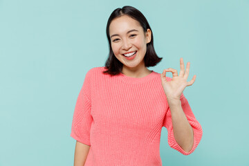 Young smiling satisfied cool happy woman of Asian ethnicity 20s wearing pink sweater showing okay...