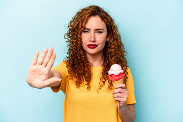 Young ginger woman holding an ice cream isolated on blue background standing with outstretched hand showing stop sign, preventing you.