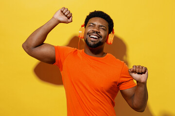 Young joyful happy fun man of African American ethnicity 20s wear orange t-shirt headphones listen...