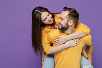 Young happy couple two friends family man woman together in yellow casual clothes look to each other giving piggyback ride to joyful, sit on back isolated on plain violet background studio portrait.