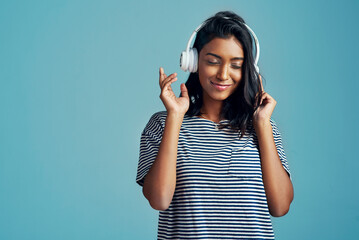 This is my kinda music. Cropped shot of a beautiful young woman wearing headphones against a blue background.