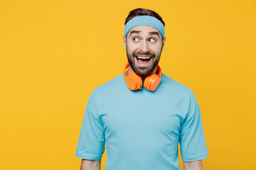 Young fitness trainer instructor sporty man sportsman in headband blue t-shirt spend weekend in home gym look aside on workspace area isolated on yellow background. Workout sport motivation concept.