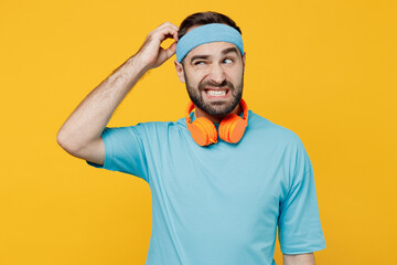 Young confused sad puzzled fitness trainer instructor sporty man sportsman in headband blue t-shirt...