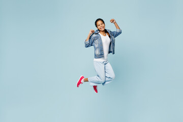 Full body excited happy little kid teen girl of African American ethnicity 12-13 years old in denim jacket jump high do winner gesture isolated on pastel plain light blue background Childhood concept