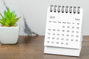 June 2022 desk calendar with plant pot on wooden table.