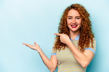 Young ginger caucasian woman isolated on blue background excited holding a copy space on palm.