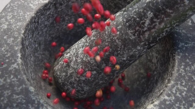 Red spicy peppercorns are falling into the grey stone mortar