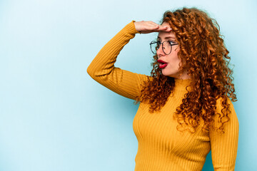 Young ginger caucasian woman isolated on blue background looking far away keeping hand on forehead. - obrazy, fototapety, plakaty