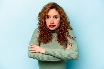 Young ginger caucasian woman isolated on blue background shrugs shoulders and open eyes confused.