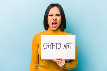 Young hispanic woman holding crypto art placard isolated on blue background screaming very angry and aggressive.