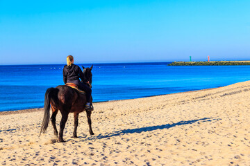 Young woman riding horse in sand beach of the Baltic sea in Darlowko, Poland