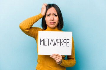 Young hispanic woman holding metaverse placard isolated on blue background being shocked, she has...