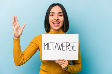 Young hispanic woman holding metaverse placard isolated on blue background receiving a pleasant...