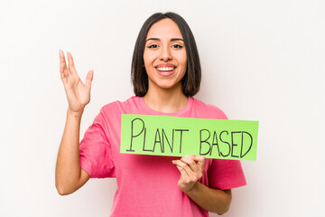 Young caucasian woman holding plant based placard isolated on white background receiving a pleasant surprise, excited and raising hands.