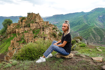 A girl on the background of Gamsutl village in the Caucasus mountains, on top of a cliff. Dagestan Russia June 2021