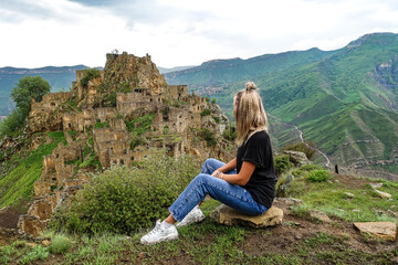 Naklejka na ściany i meble A girl on the background of Gamsutl village in the Caucasus mountains, on top of a cliff. Dagestan Russia June 2021