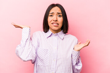 Young hispanic woman isolated on pink background confused and doubtful shrugging shoulders to hold...