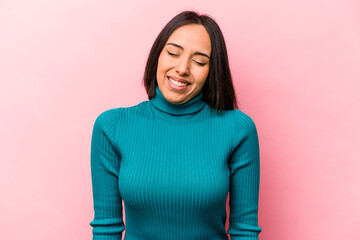 Young hispanic woman isolated on pink background laughs and closes eyes, feels relaxed and happy.