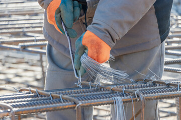 A worker uses steel tying wire to fasten steel rods to reinforcement bars. Close-up. Reinforced concrete structures - knitting of a metal reinforcing cage.