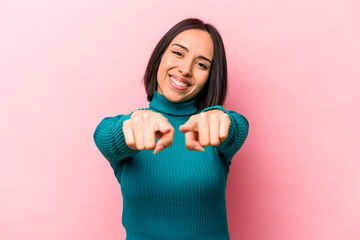 Young hispanic woman isolated on pink background pointing to front with fingers.
