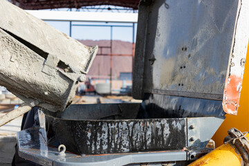 A concrete mixer truck pours mortar into a concrete pump at a construction site. Supply of concrete and mortar for the production of monolithic reinforced concrete works. Close-up.