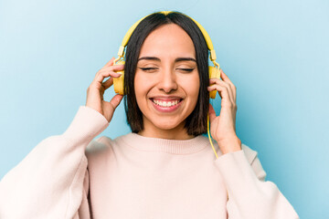 Young hispanic woman listening to music isolated on blue background